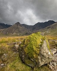 A massive boulder covered in moss with mountains behind at Coire na Creiche, Isle of Skye