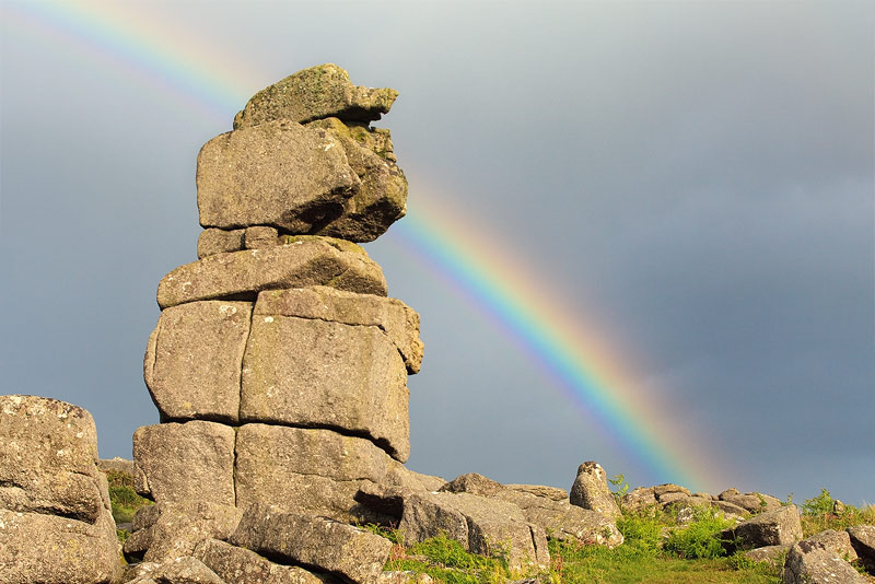 A rainbow forms behind Bowermans Nose on Dartmoor