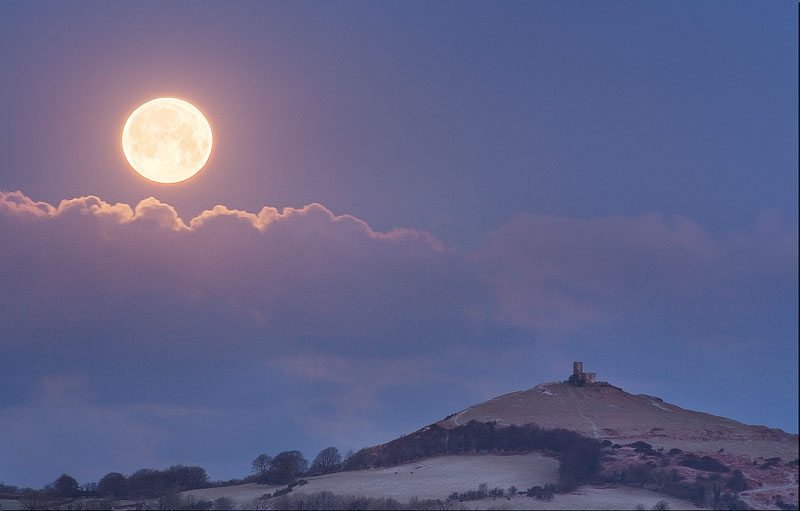 the moon setting at sunrise next to Brentor Church in Devon
