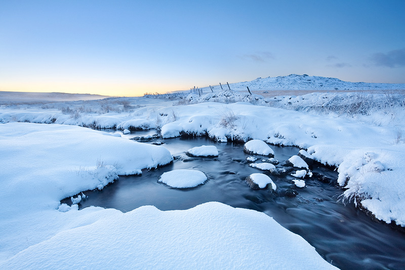 dawn on a stream flowing between snow on dartmoor